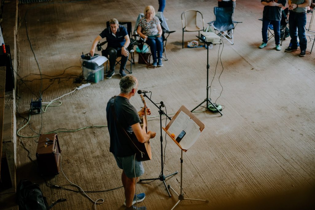 A musician performs with an acoustic guitar in front of an audience.