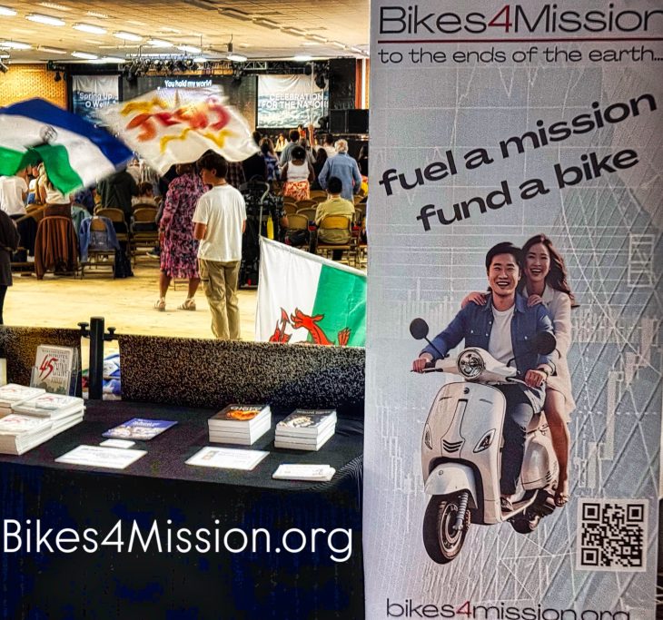 A busy event with people, flags, and a display for Bikes4Mission promoting bike donations.