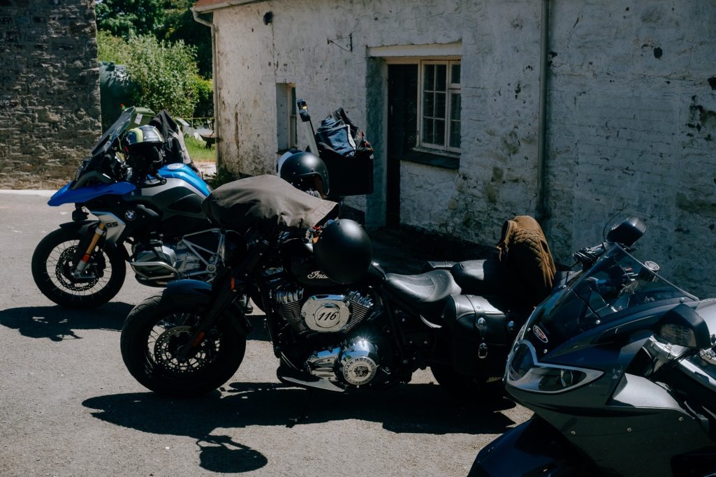 Three parked motorcycles outside a rustic building with a greenery backdrop.